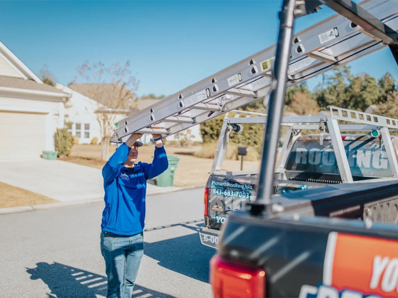Roofing inspector unloading a ladder from a work truck.