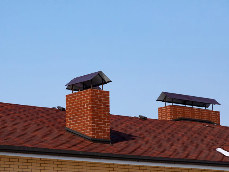 Brick chimneys with metal flashing on a sloped roof.