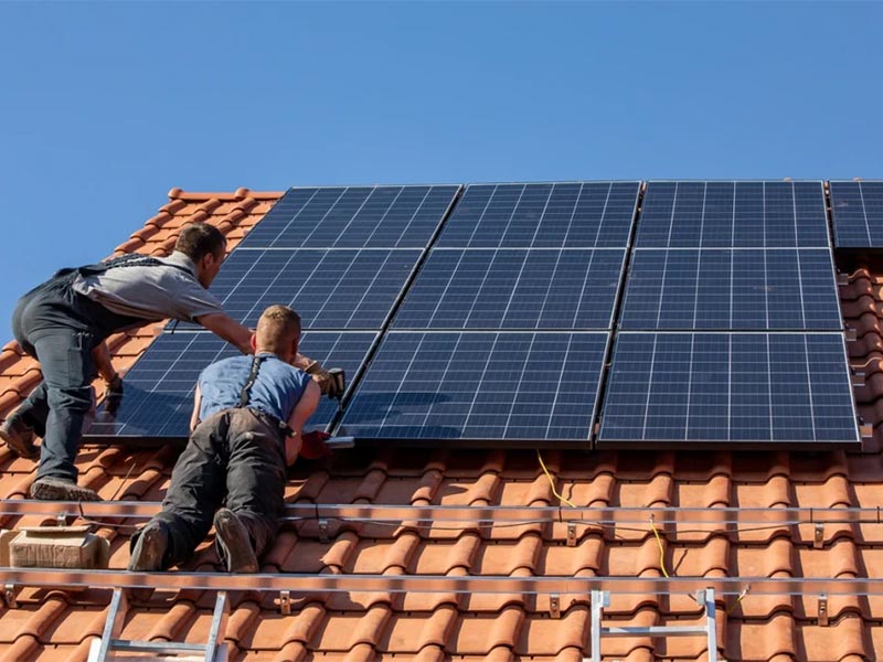 Workers installing solar panels on a tiled roof.