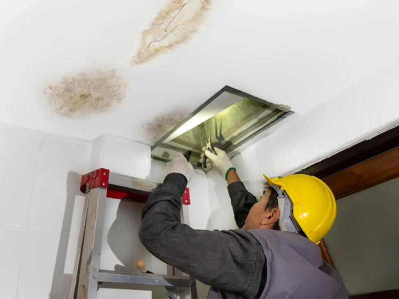 Worker repairing a ceiling leak near an attic opening.