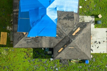 arial view of a damaged roof with blue tarping covering the upper portion