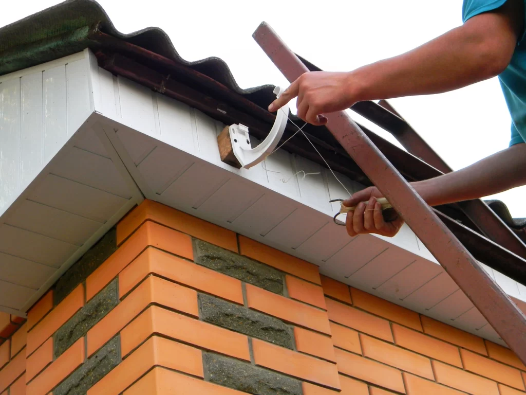 brick house with roofing contractor repairing roof fascia