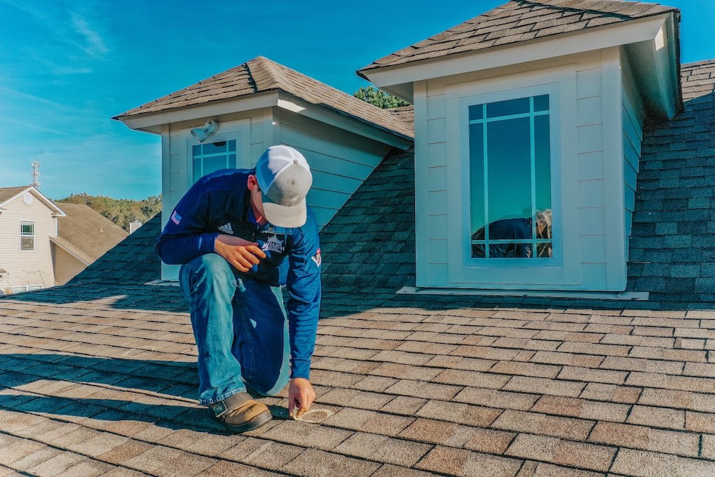 man on roof marking storm damage to determine roof repair cost