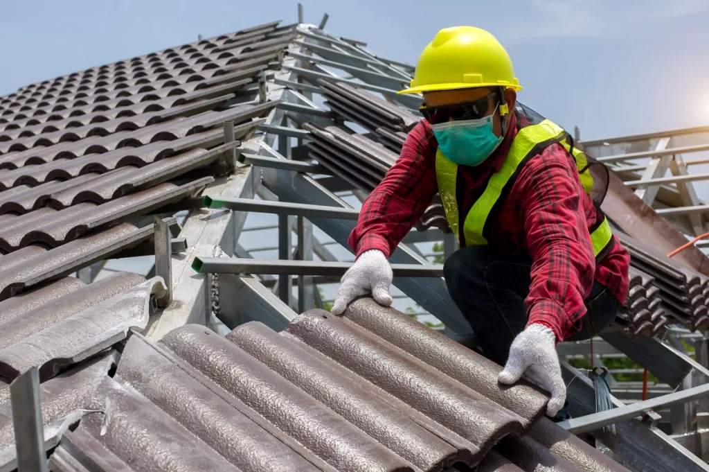 worker in safety gears placing new roof tiles